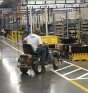 A man is riding a lawn mower in a warehouse.