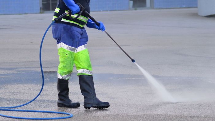 A man is using a high pressure washer on a concrete surface.