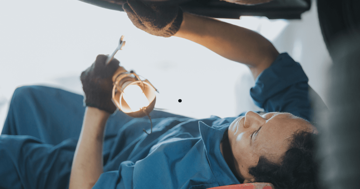 a mechanic under a car with a light inspecting it