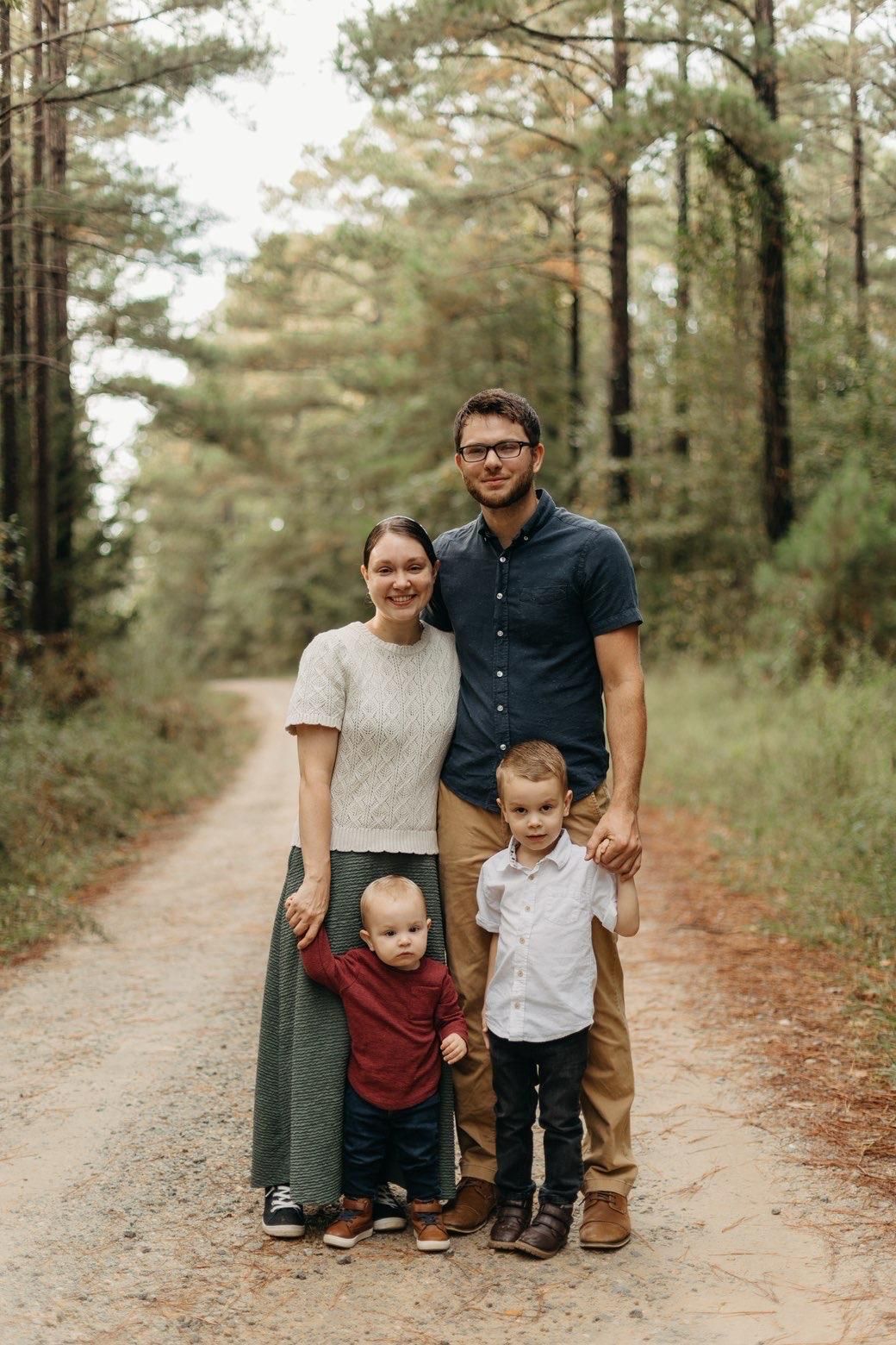 A person in a white long-sleeved shirt kneels on a roof, using a pneumatic nail gun to install asphalt shingles.