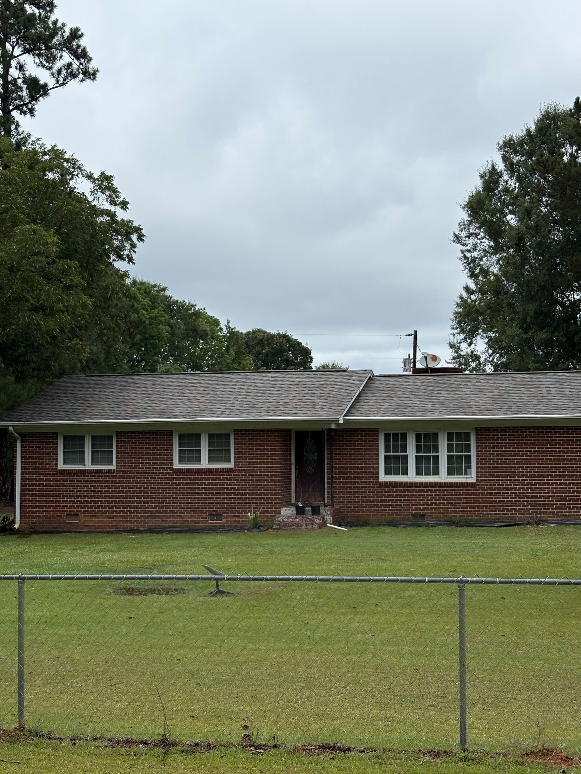 A brick house exterior with gray shingles, beige siding in the gables, and metal gutters installed on the corner.