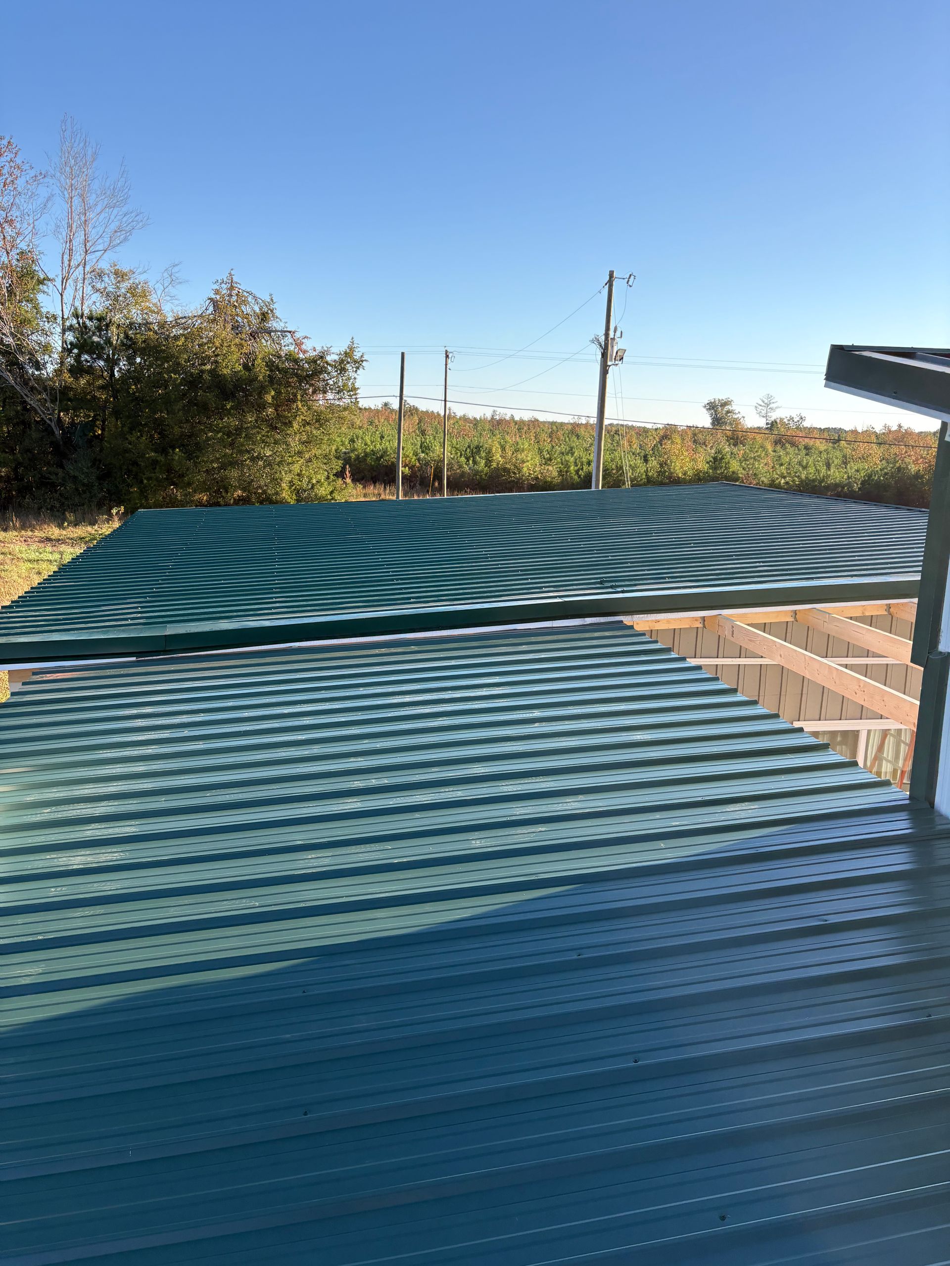 A worker in high-visibility gear uses a yellow drill to attach metal roofing panels, with a hard hat and screws nearby.