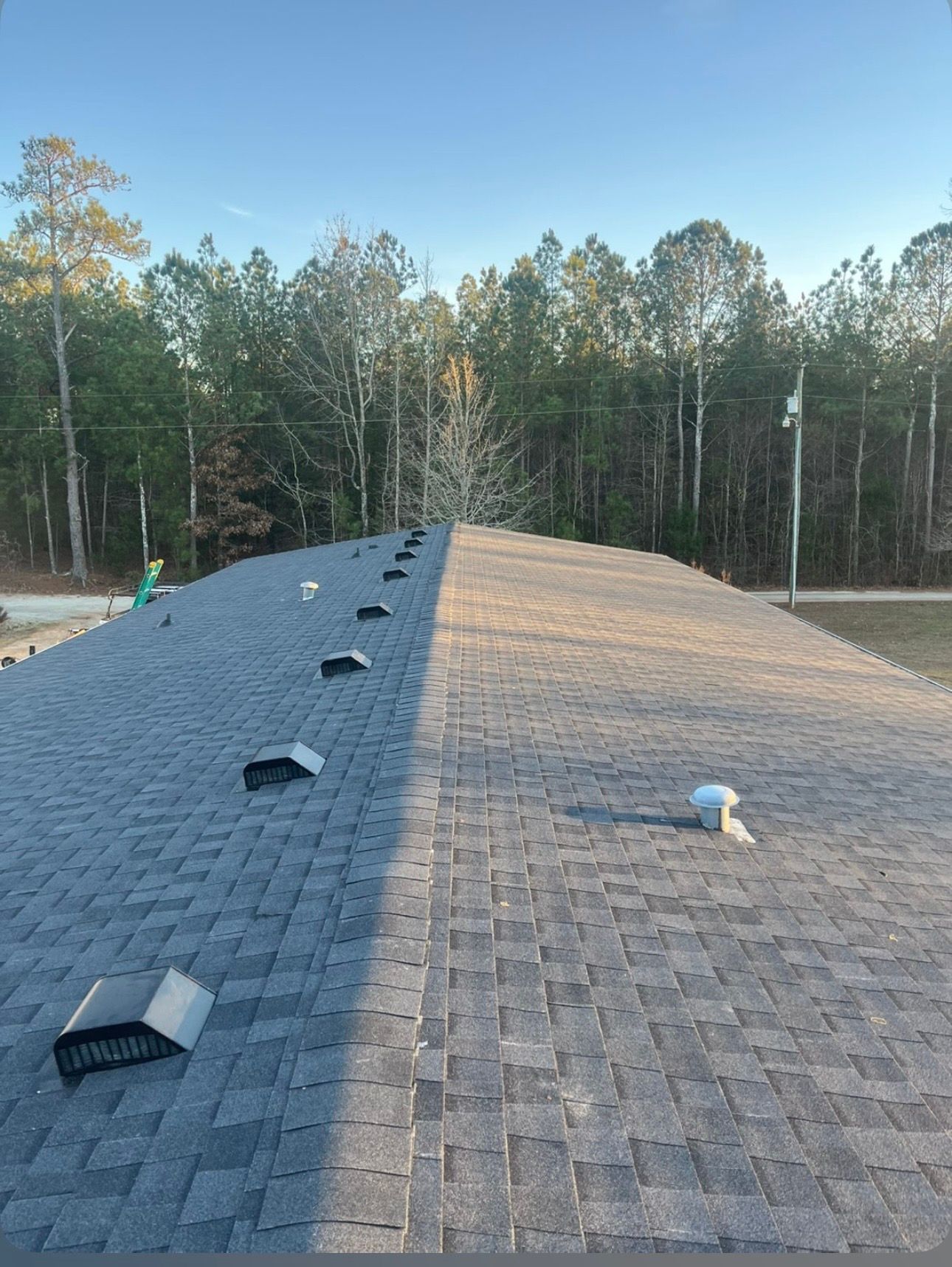 A person in work clothes uses a drill to install a red roof tile on a sloped residential roof.