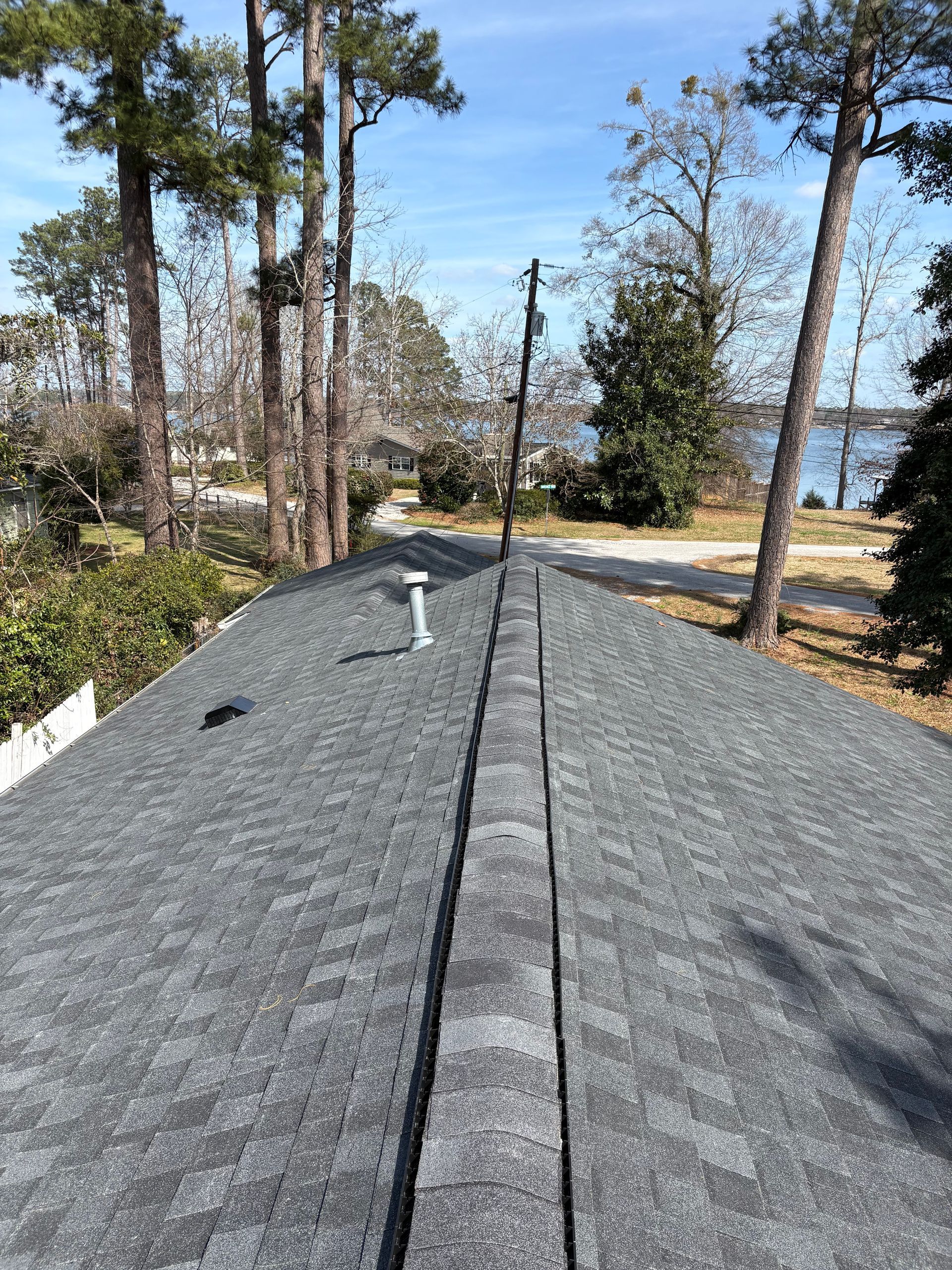 A worker in workwear uses a power drill to install metal roofing panels on a sloped residential roof.