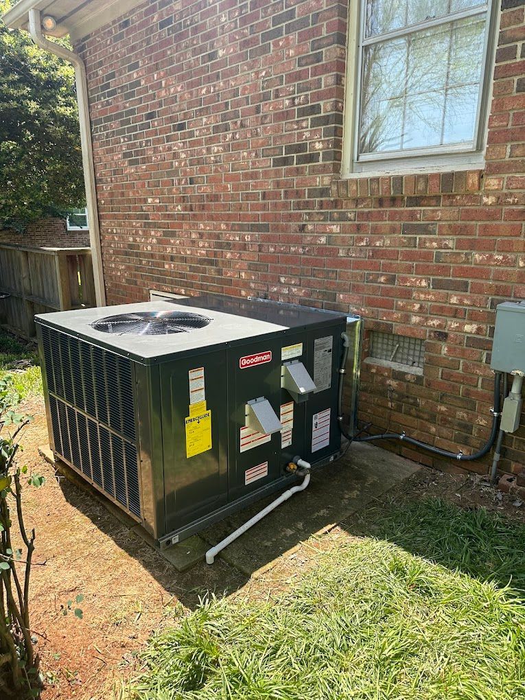 A black air conditioner is sitting on the side of a brick house.