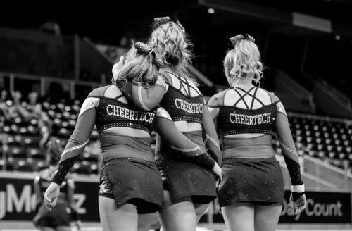 Three cheerleaders are standing next to each other in a stadium.