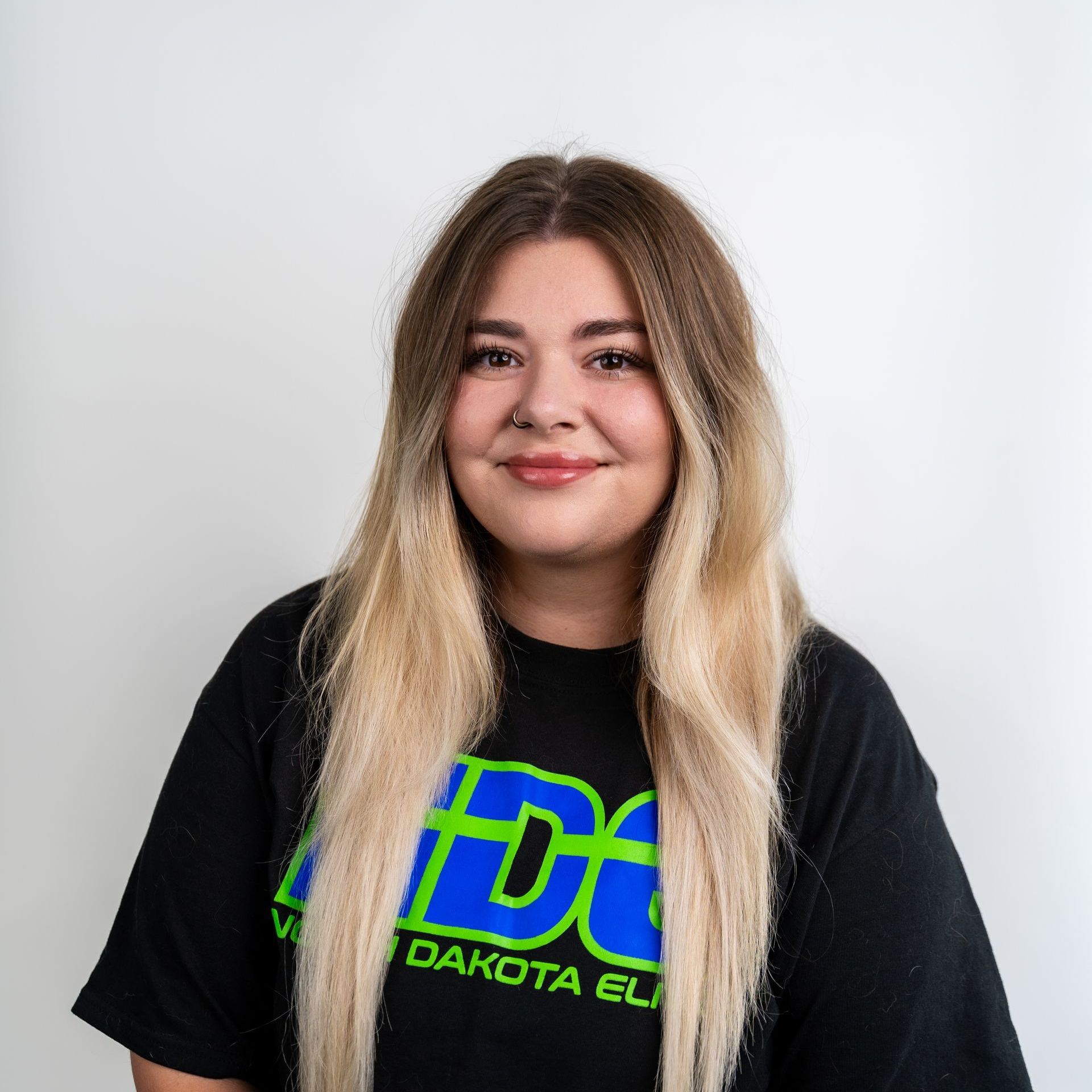 A woman is sitting in a green chair wearing a black shirt with the word dakota on it.