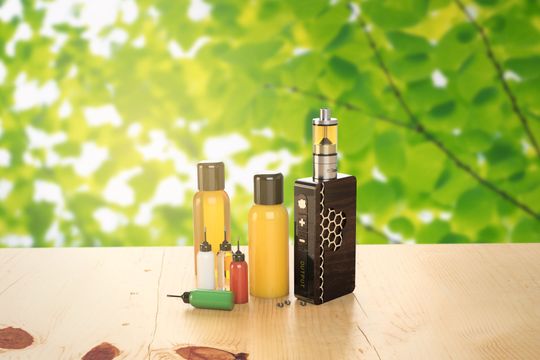 Dispositivo per svapare e flaconi di e-liquid su una superficie di legno, sfondo di fogliame verde.