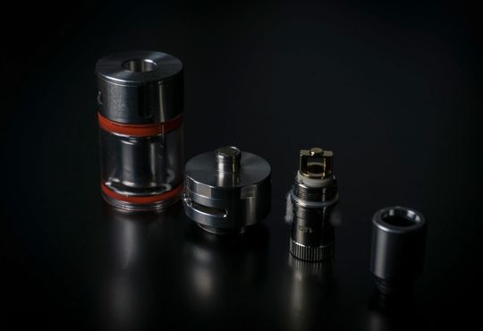 Parti del dispositivo per lo svapo, smontate e disposte su una superficie nera. Include un serbatoio, un atomizzatore e altri componenti.