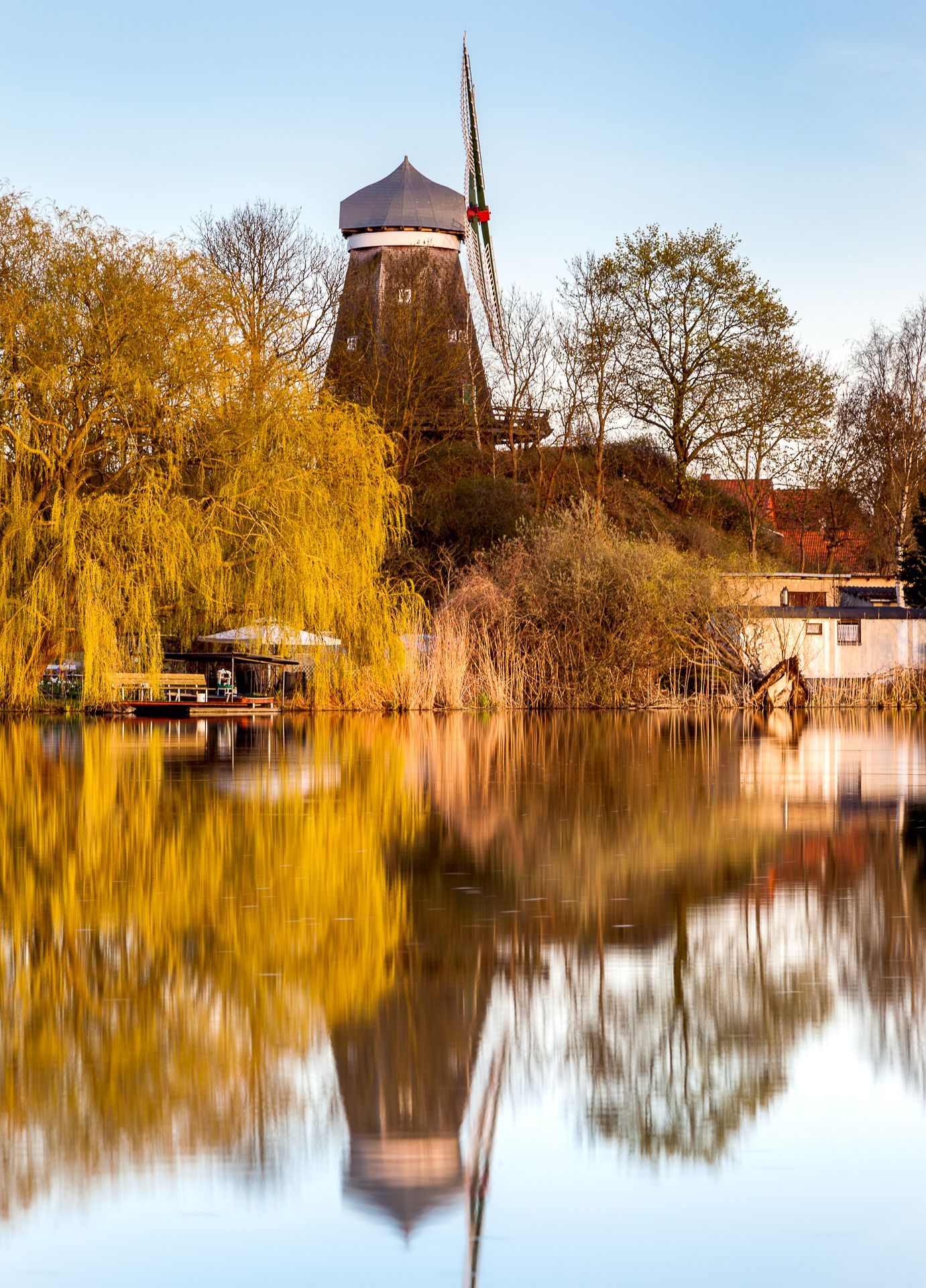 Windmühle spiegelt sich im ruhigen Wasser mit herbstlichem Laub.