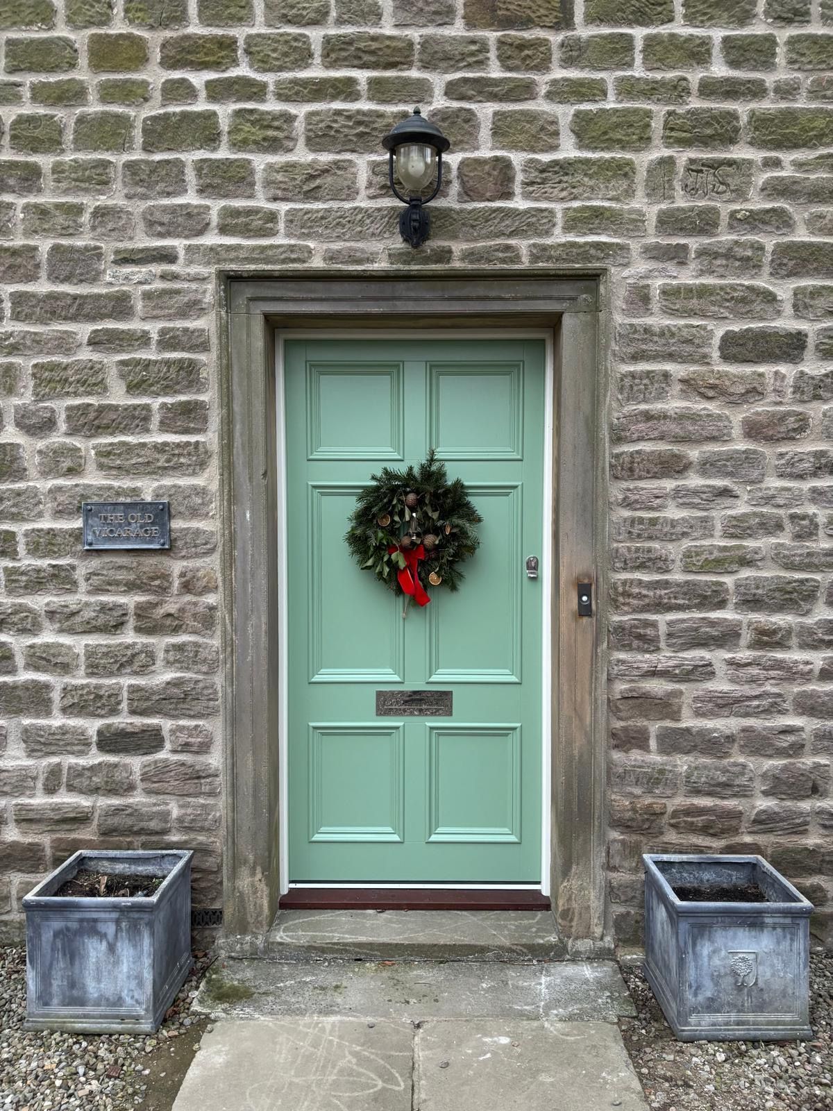 A green door with a wreath on it is on a brick building.