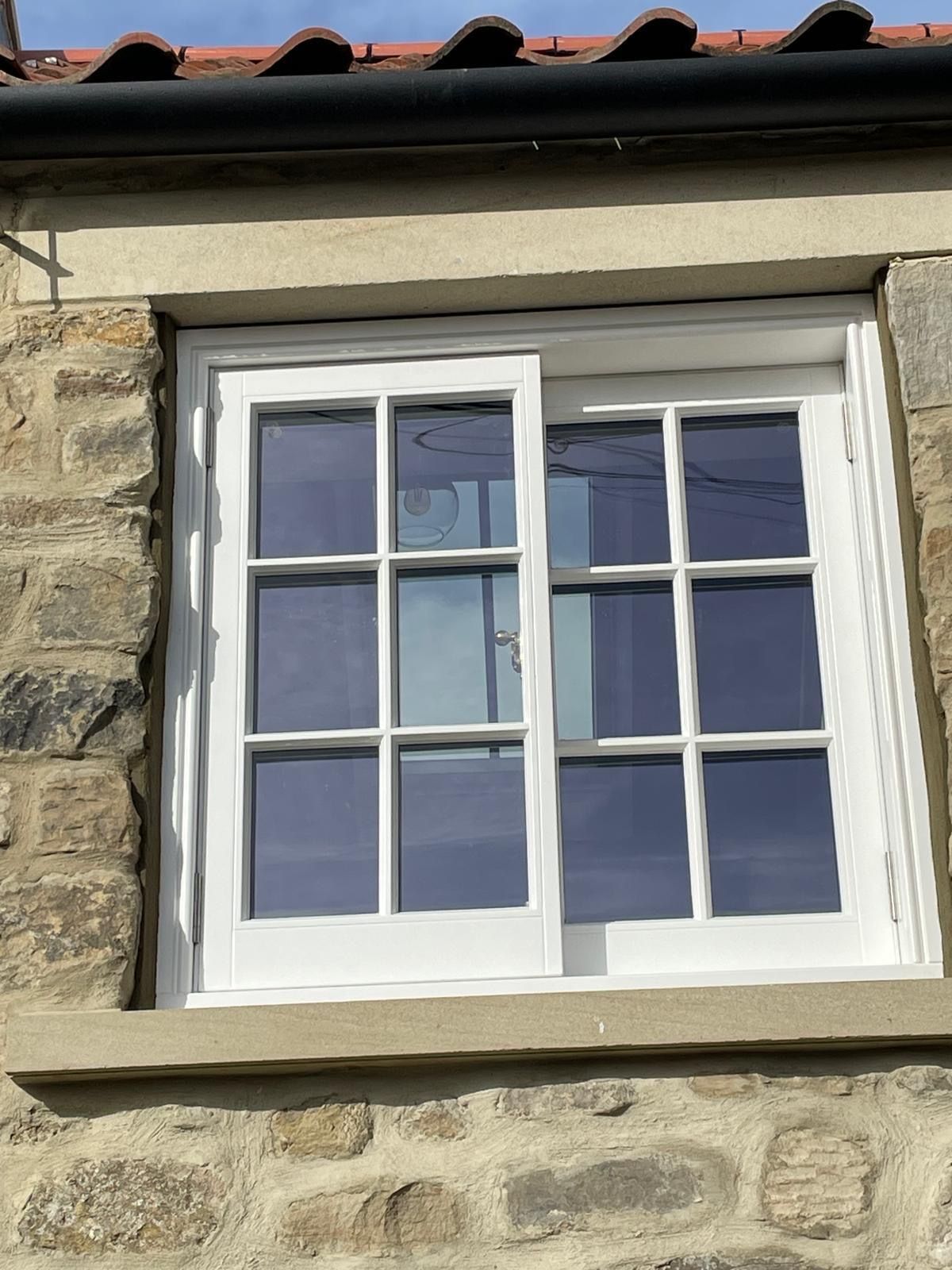 A white window is on the side of a stone building.