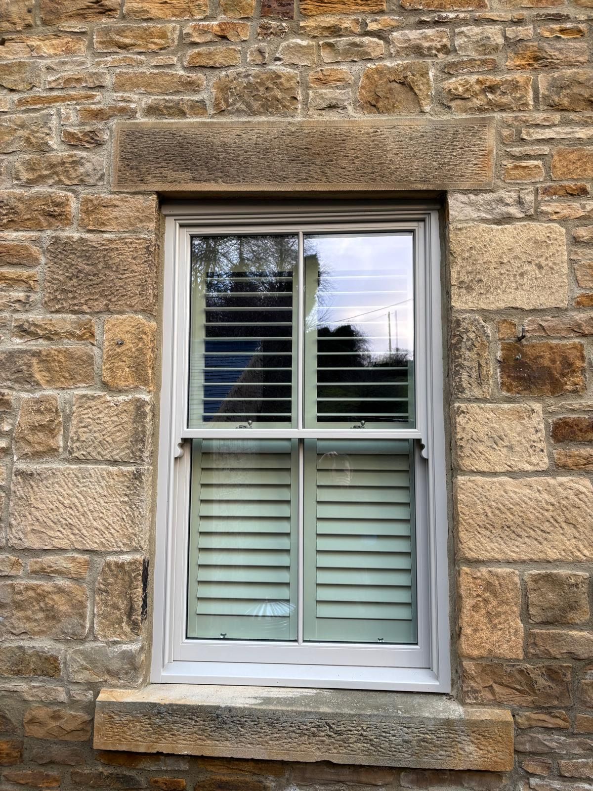 A window with shutters on it is on a stone wall.
