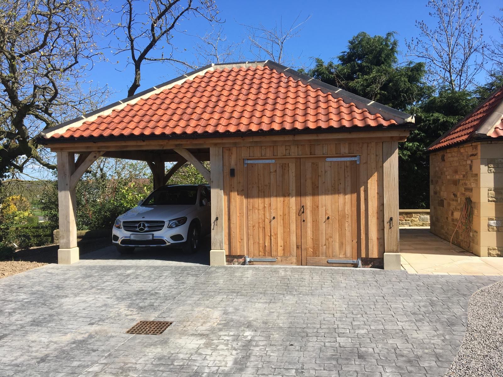A white car is parked under a wooden garage with a tiled roof.