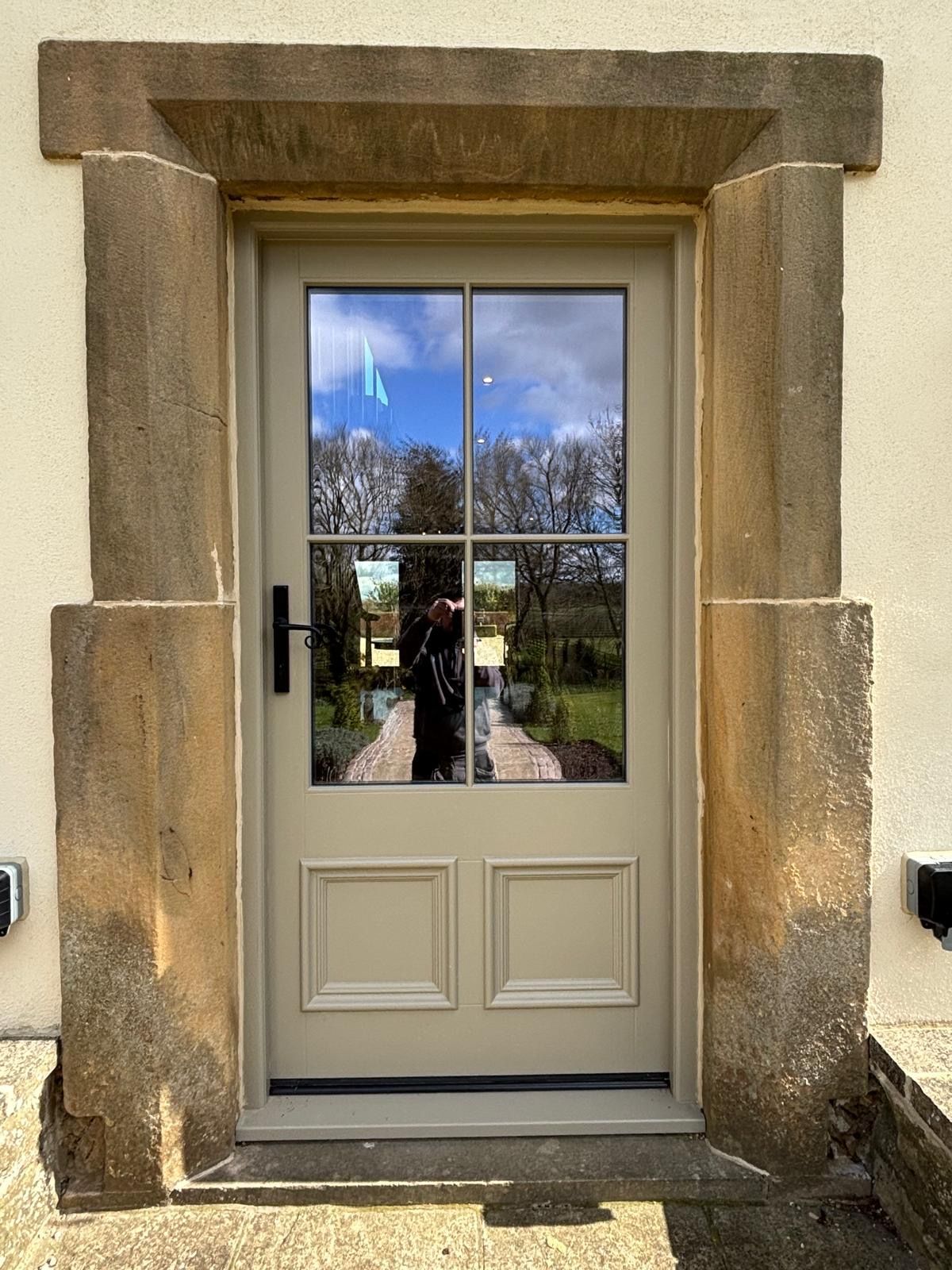 A door with a reflection of a person in it is on the side of a building.
