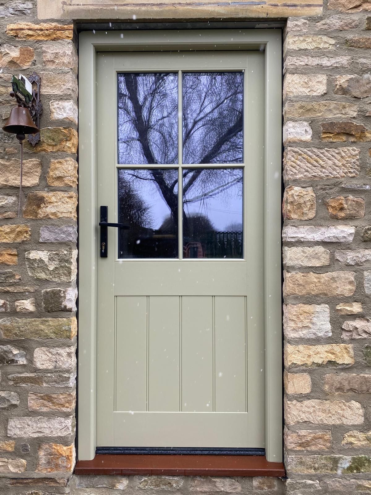 A green door with four windows is on a stone wall.