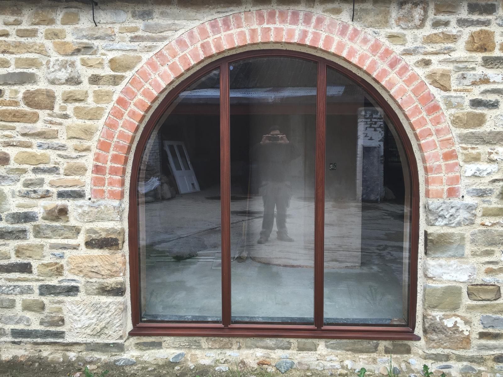 A brick building with a large arched window and a reflection of a person in the window.