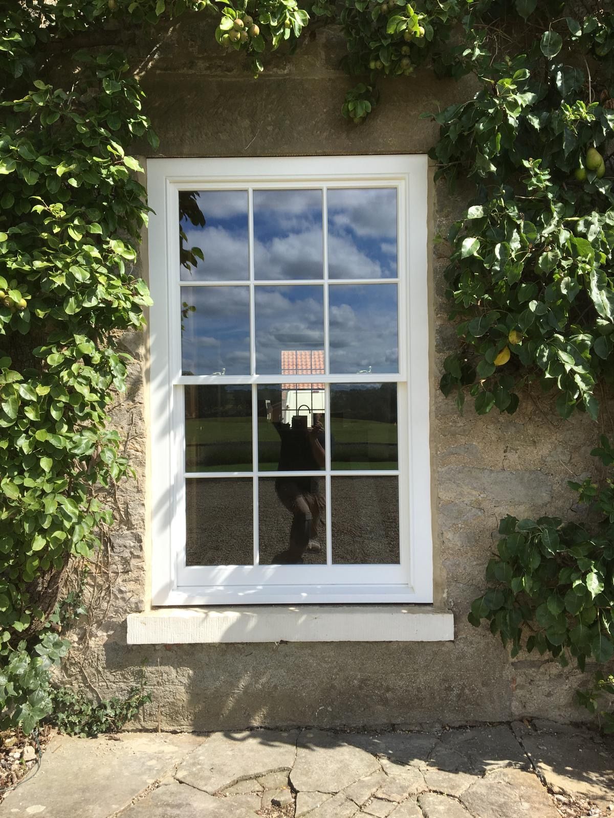 A white window on a stone wall with a reflection of a person in the window.