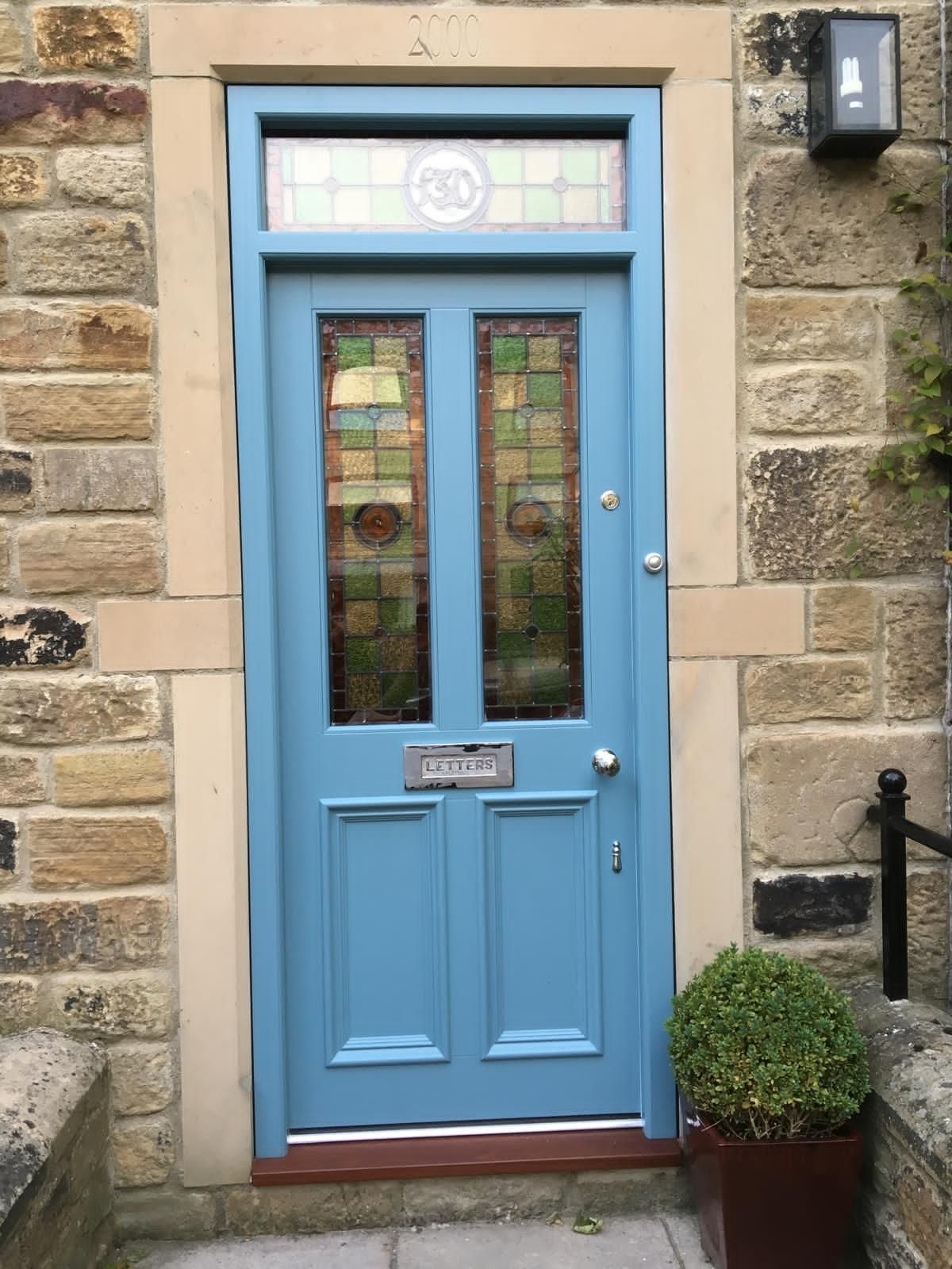 A blue door with a stained glass window is on a stone wall.