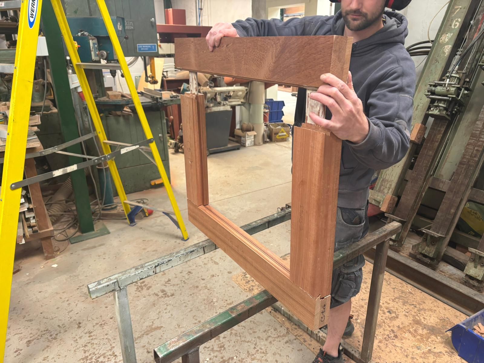 A man is holding a piece of wood in a workshop.