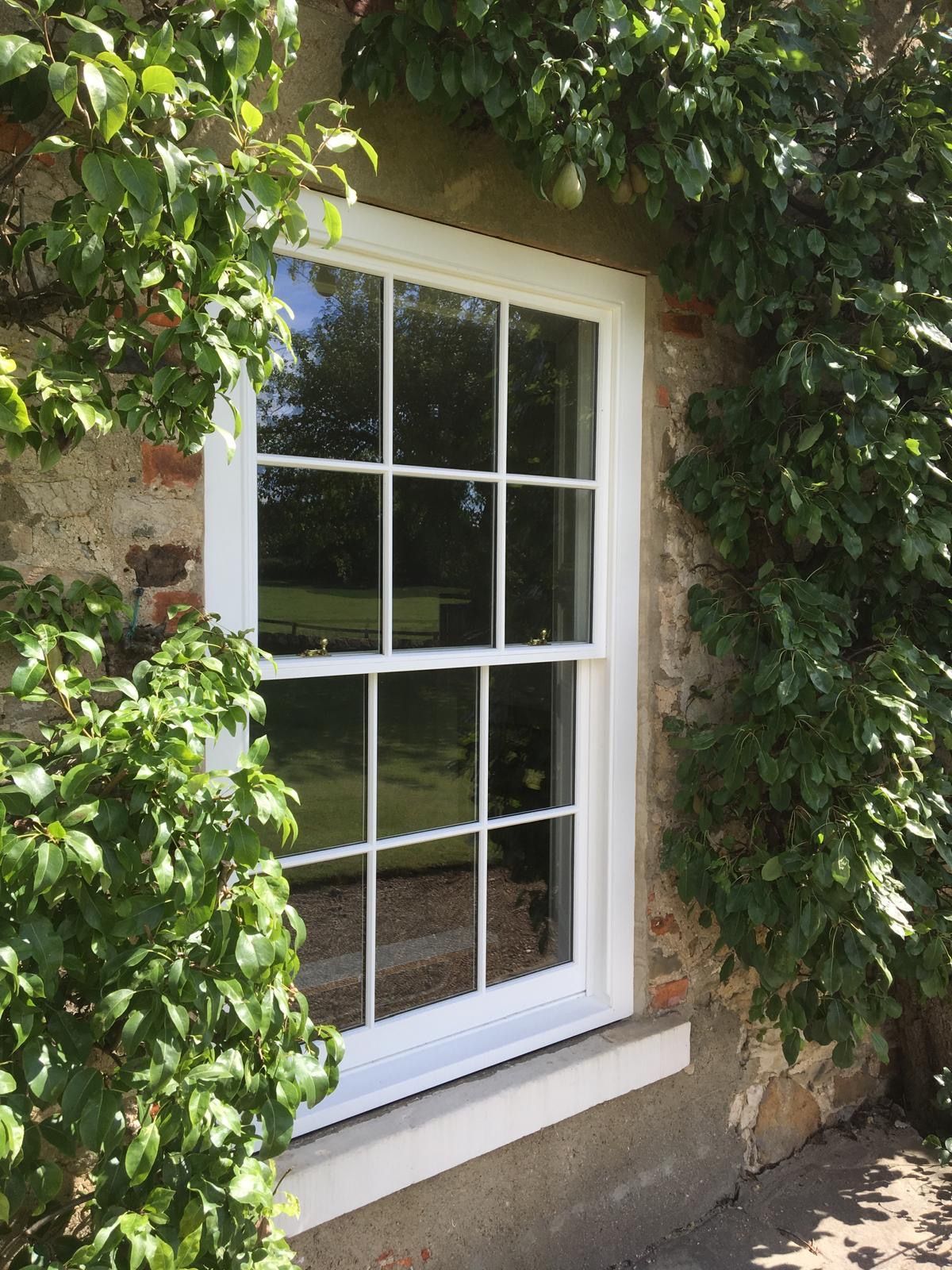 A white window is on the side of a brick building surrounded by trees.