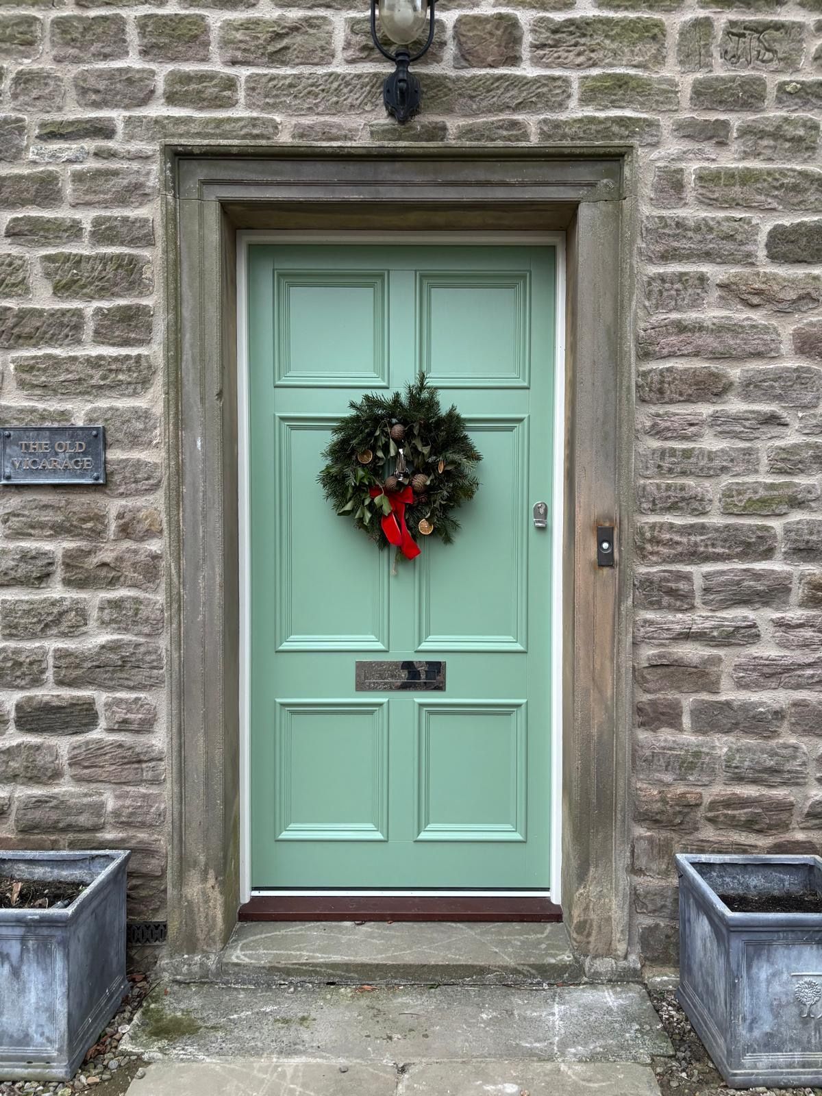 A green door with a christmas wreath on it is on a brick building.