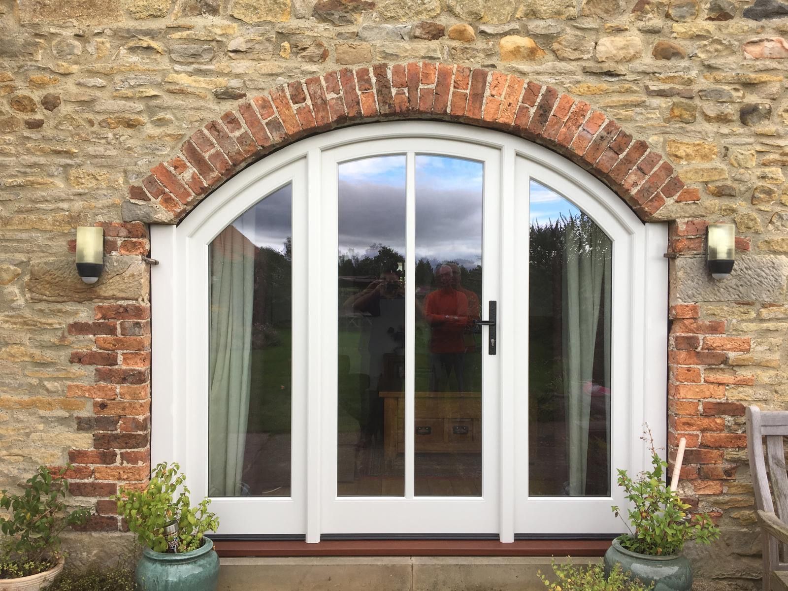 A white door with a brick arch on the side of a stone building.