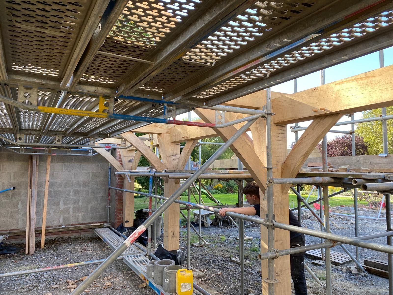 A man is working on a wooden structure under a scaffolding.