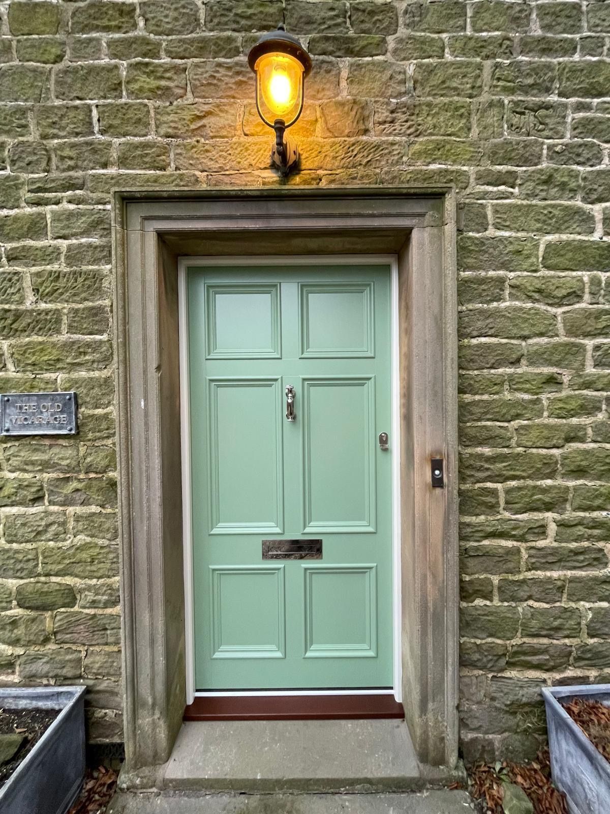 A green door is on a brick building with a lamp above it.