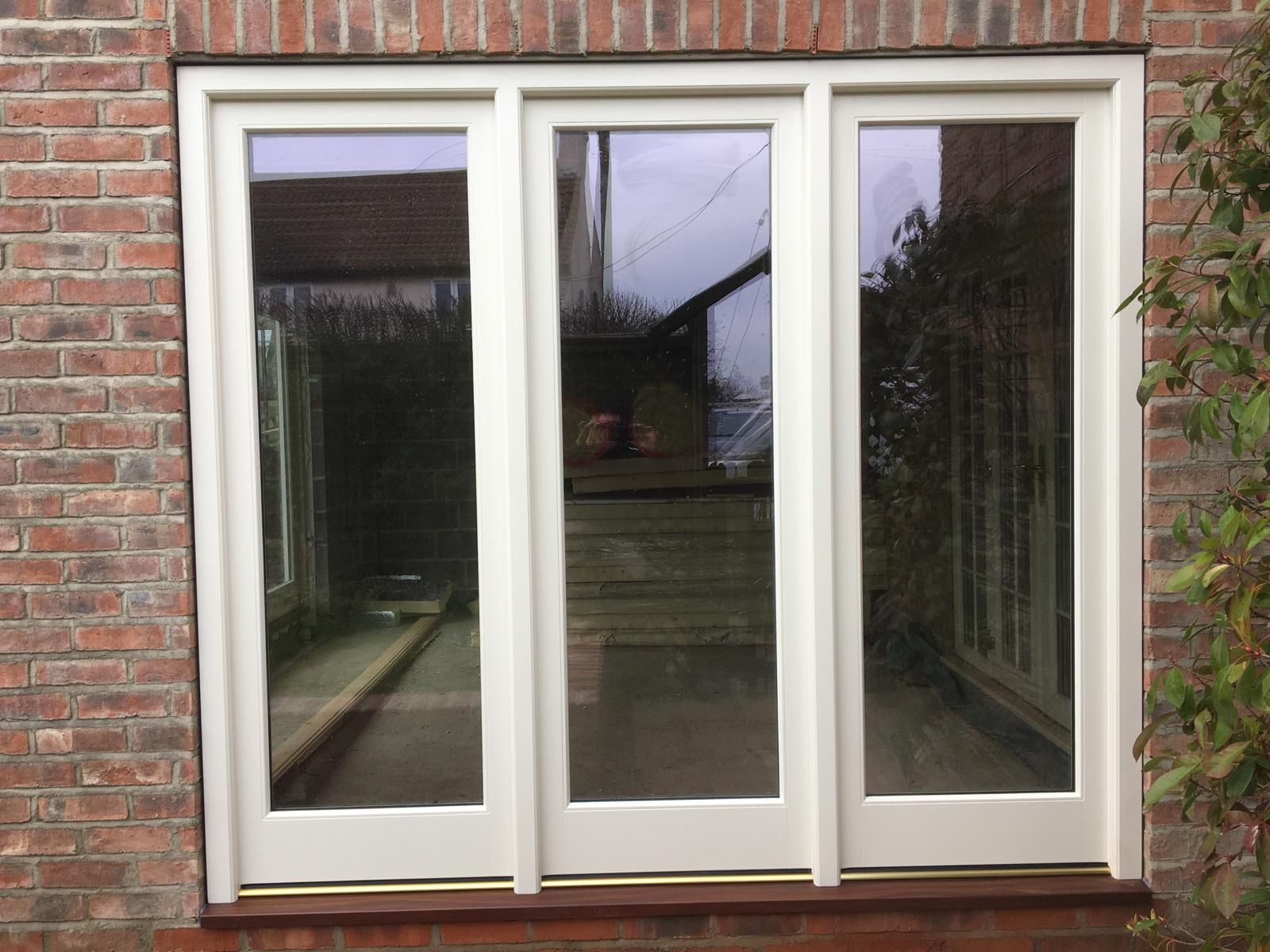 A white window with three doors on a brick wall.