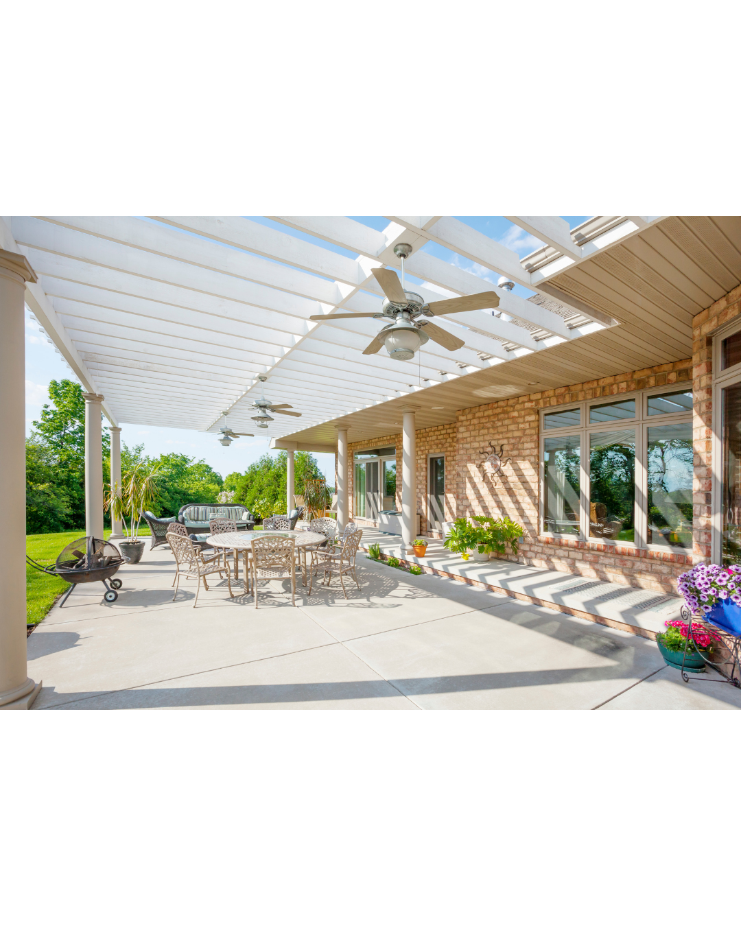 A large patio with tables and chairs under a pergola with a ceiling fan.