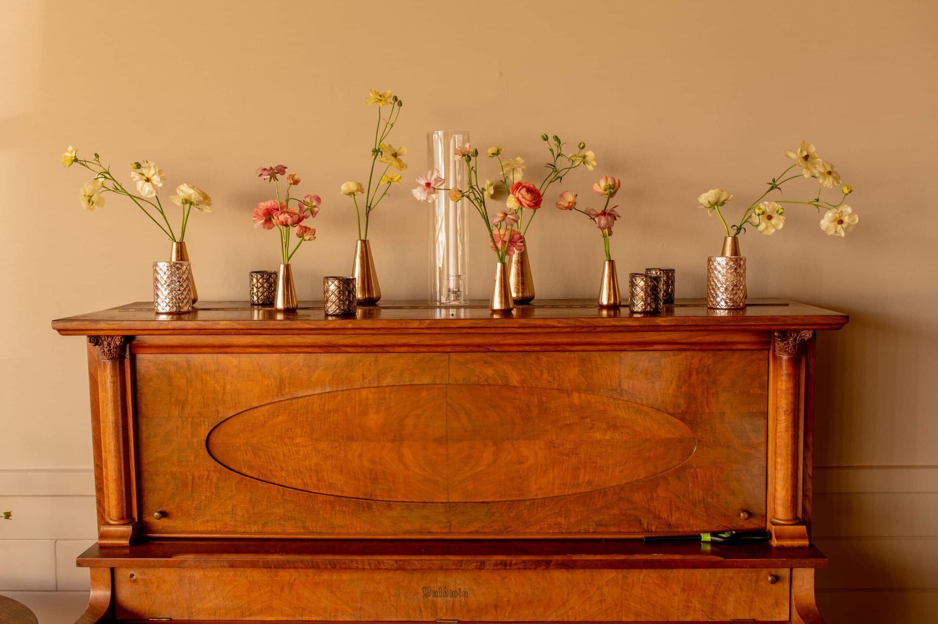 Piano top decorated with assorted flowers in small vases and candles.