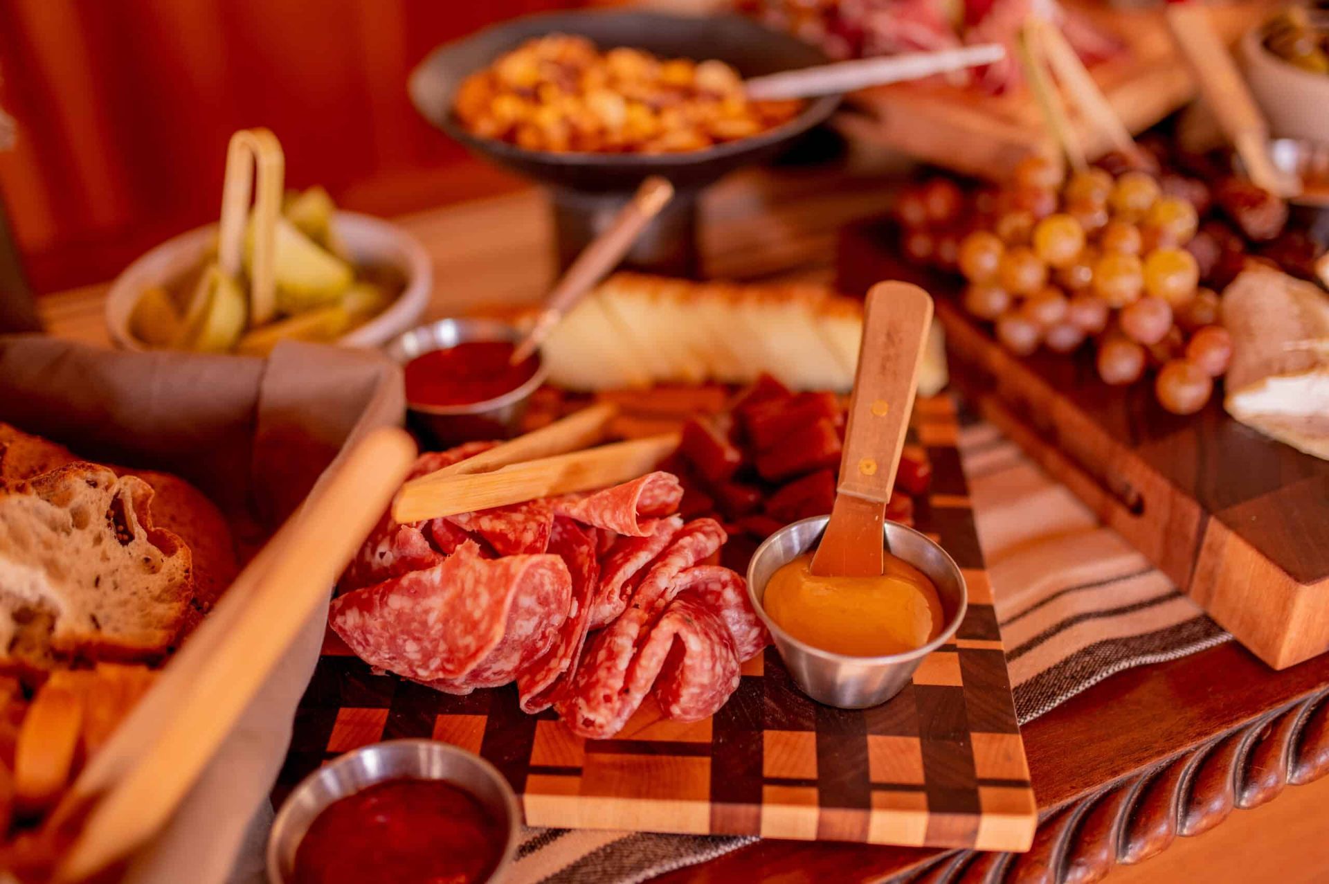 Charcuterie board with meats, cheeses, grapes, and bread, with dipping sauces and pickles.