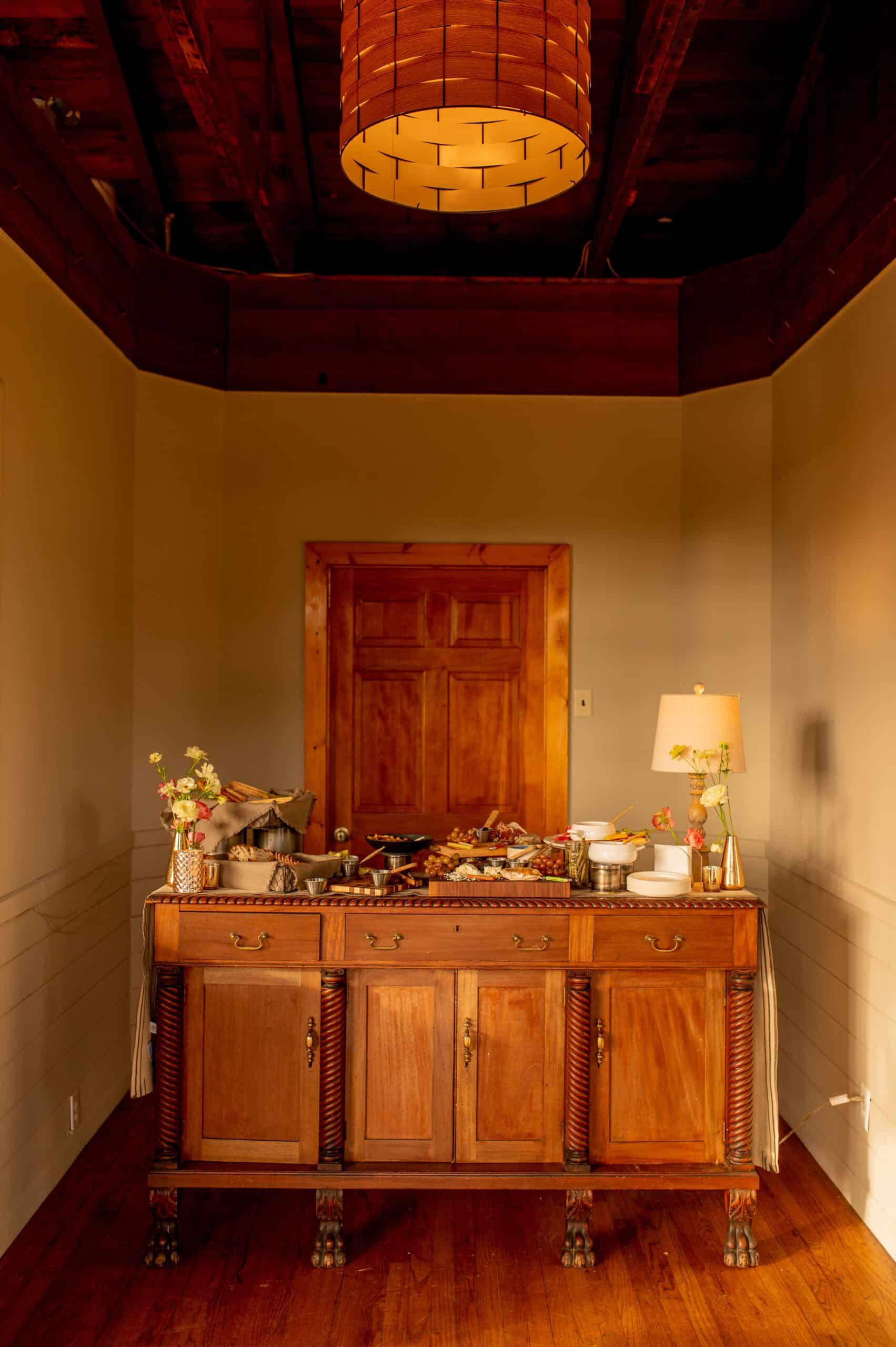 Wooden buffet with food and lamp, against a doorway, under a ceiling fixture.