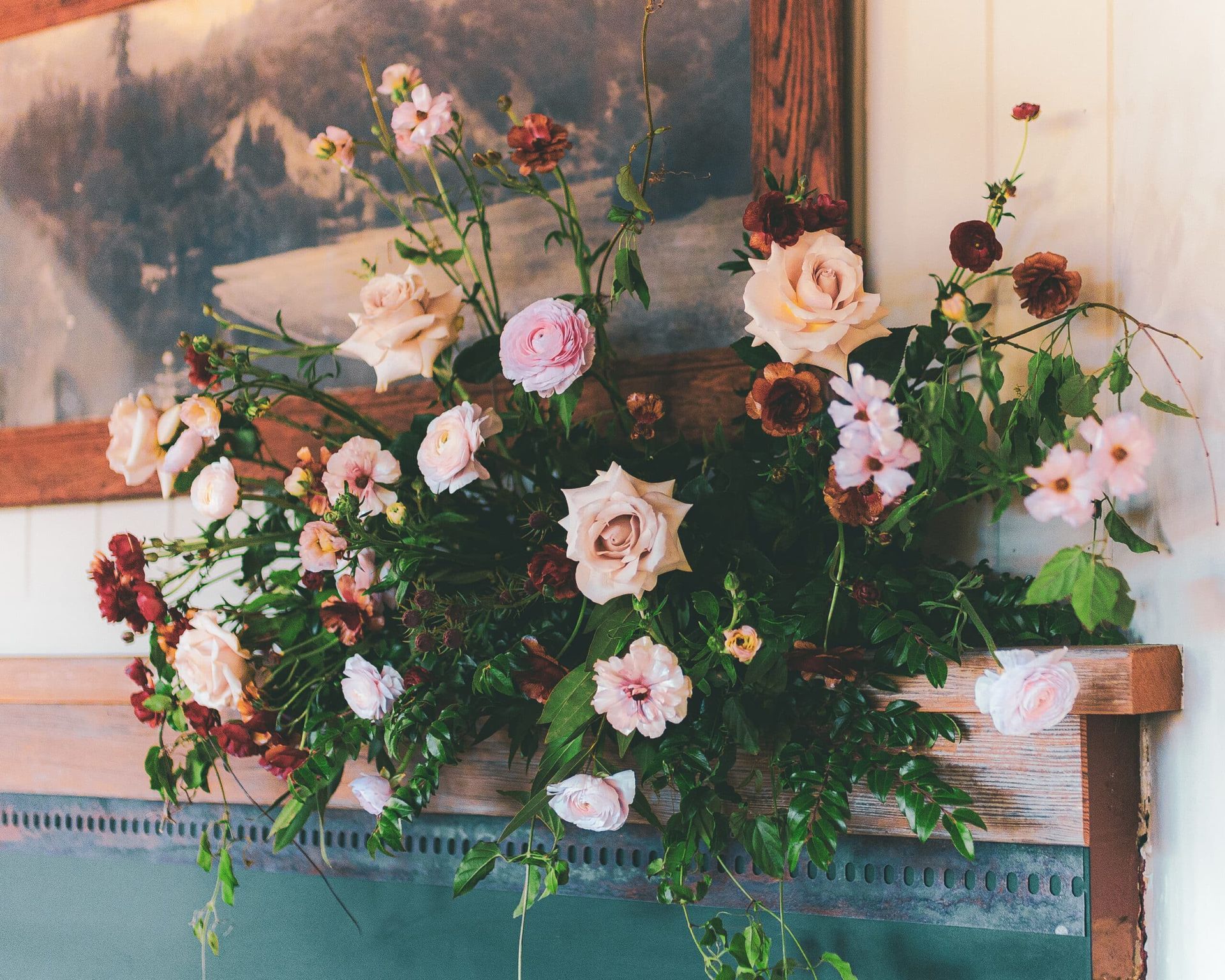 Floral arrangement with pink and cream roses, dark berries, and greenery on a wooden mantel.