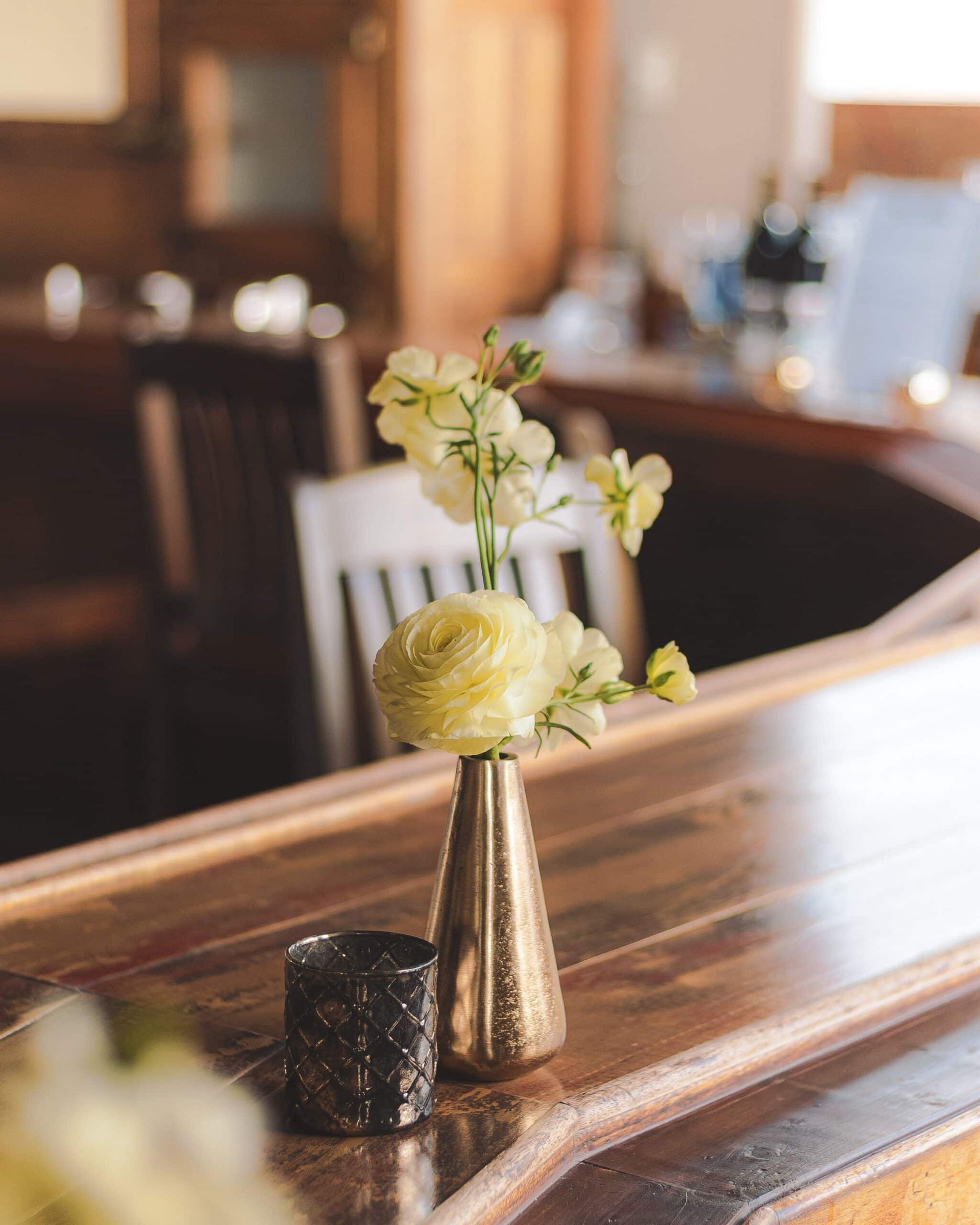 Yellow flowers in a gold vase on a wooden bar with a candle.