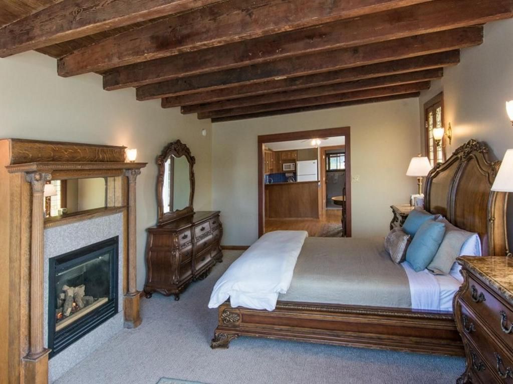 Bedroom with exposed wood beams, fireplace, ornate wooden bed frame, dresser, and mirror.