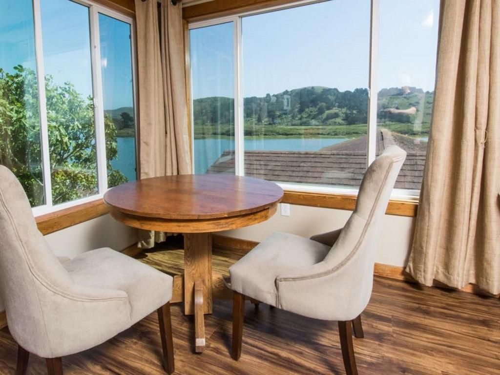 Round table with two chairs by a window overlooking a lake and trees.