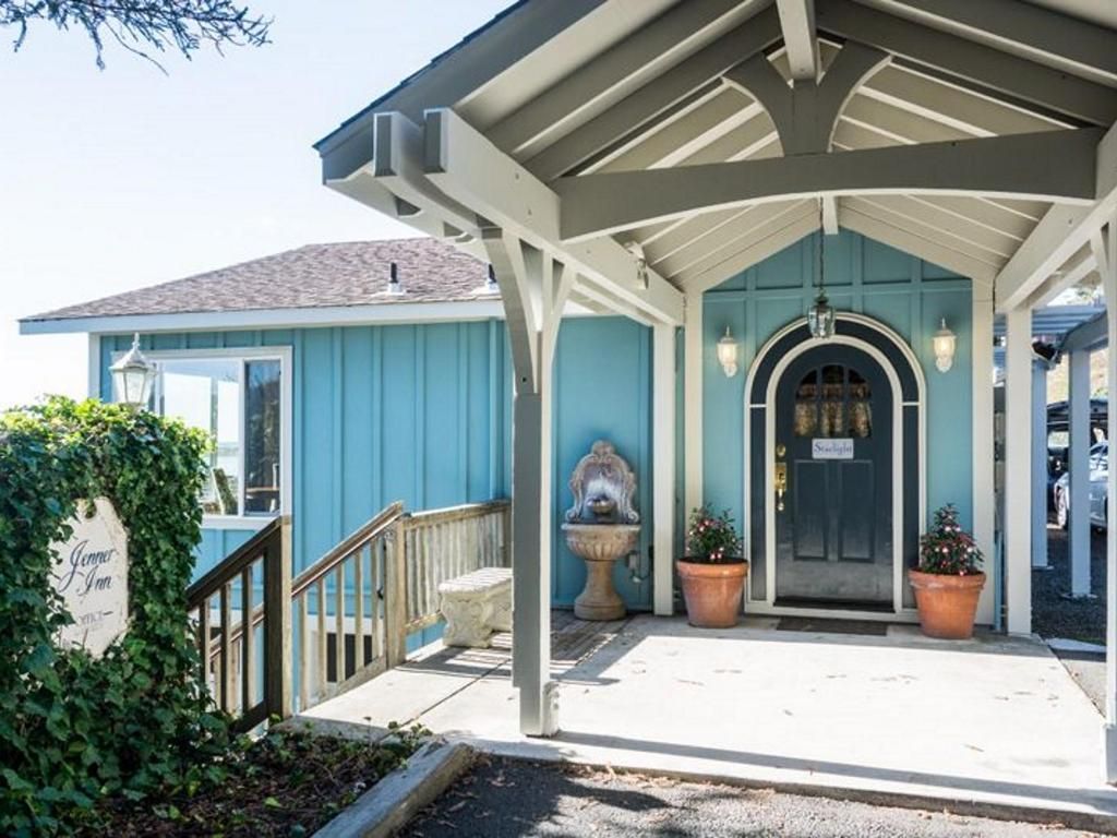 Blue building with white trim, covered entryway, and a dark door; potted plants flank the entrance.