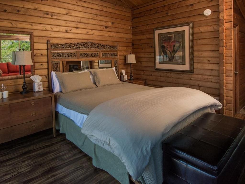 Bedroom with wood-paneled walls, bed with beige bedding, and a brown leather ottoman.