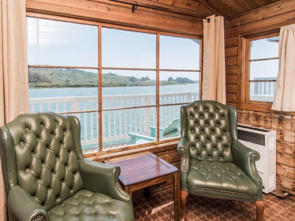 Two green leather chairs by a window overlooking a waterway. Small wooden table. Wood-paneled walls.