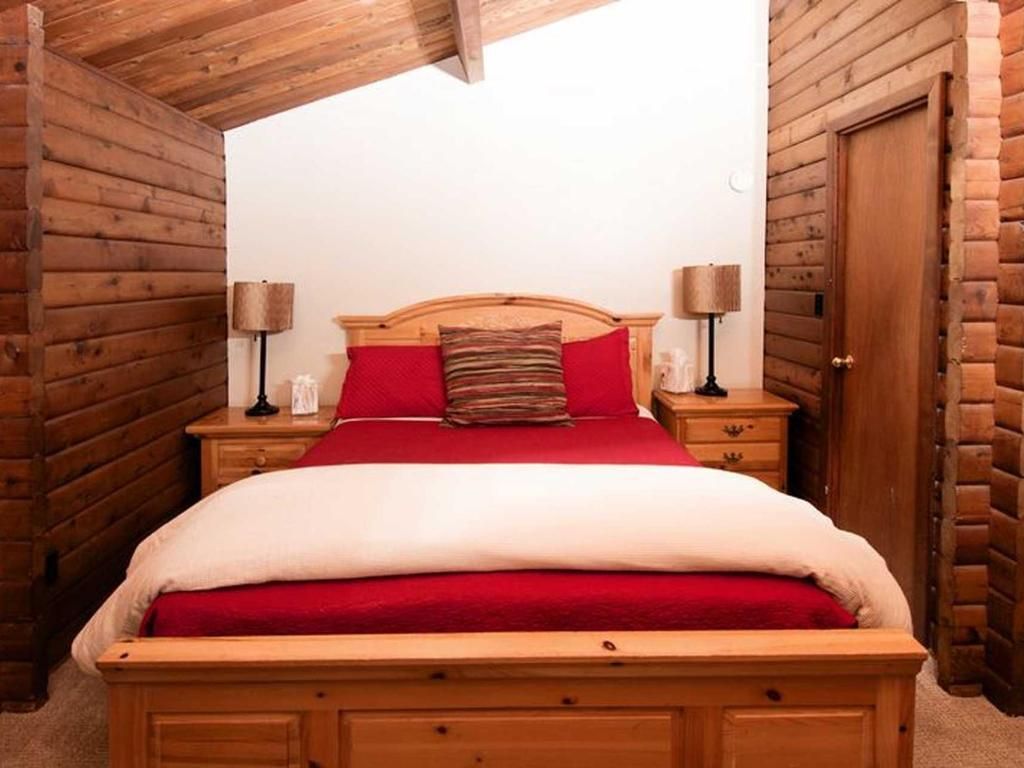 Bedroom with wooden bed frame, red bedding, and wood-paneled walls.
