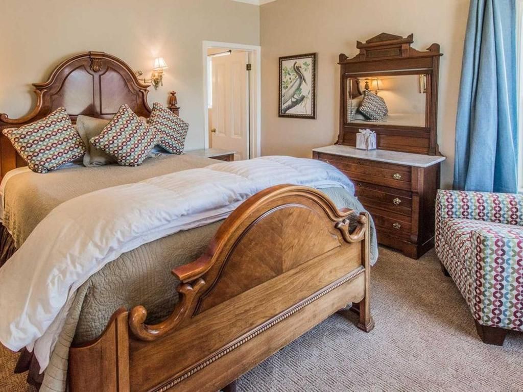 Bedroom with two ornate wooden beds, a dresser with mirror, and patterned armchair.