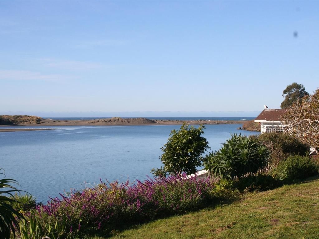 Calm water and blue sky with a view of a house and lush greenery.