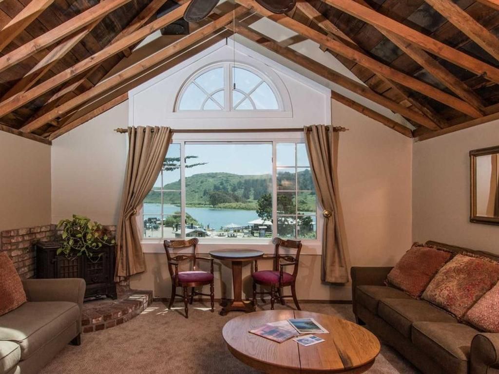 Cozy living room with lake view: couches, table, chairs, fireplace, arched window, and exposed wood ceiling.