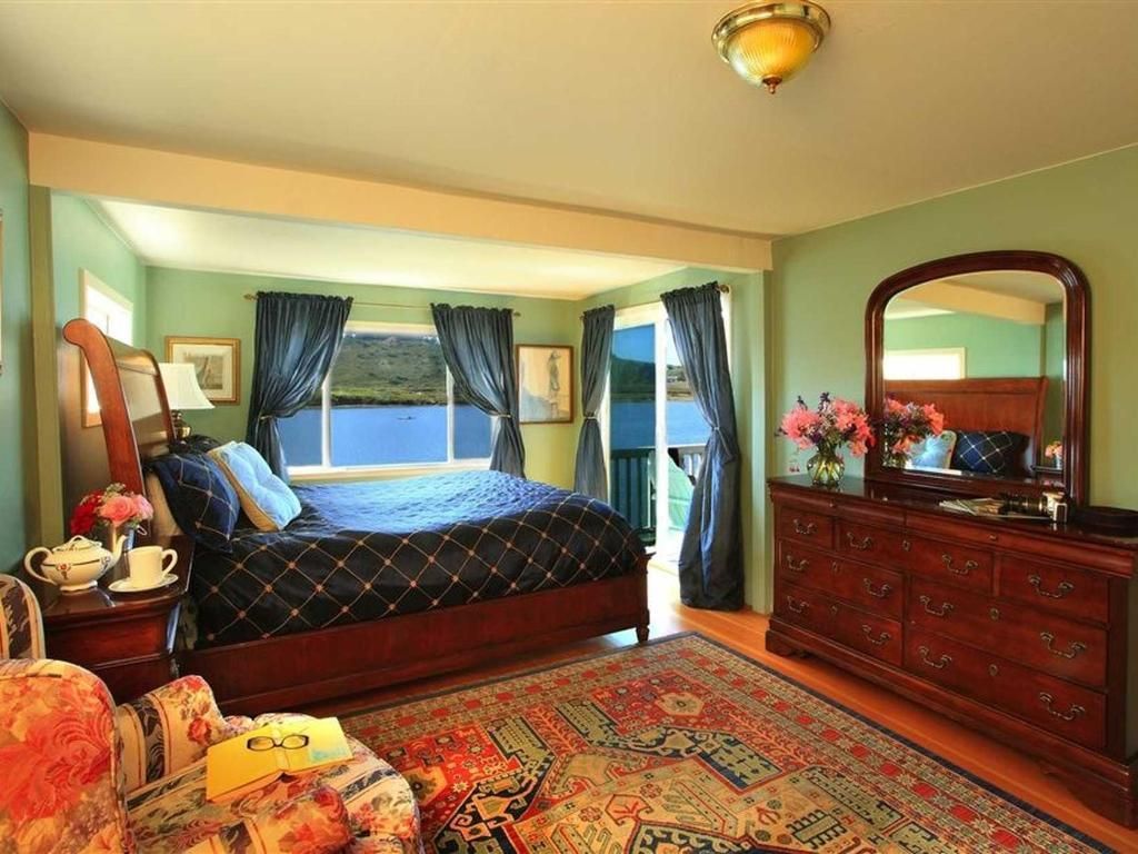 Bedroom with bed, dresser, chair, window with blue curtains, and a view of water.