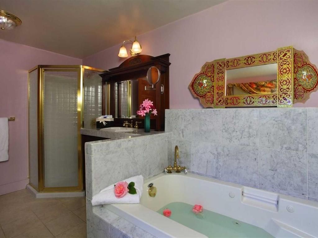 Bathroom with tub, shower, sink, mirror, and pink walls. Tub has rose petals, gold accents.