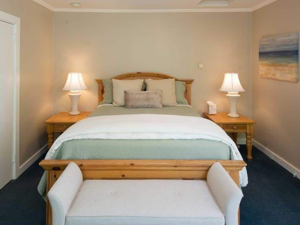 Bedroom with a bed, nightstands, lamps, and a bench. Walls are beige, bed has green and white bedding.