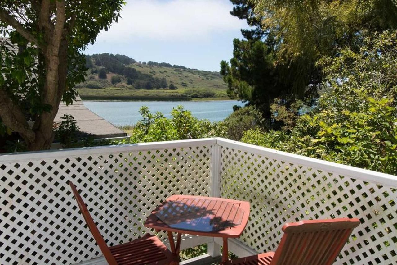A small deck with a table and chairs overlooks a lake and distant hills on a sunny day.