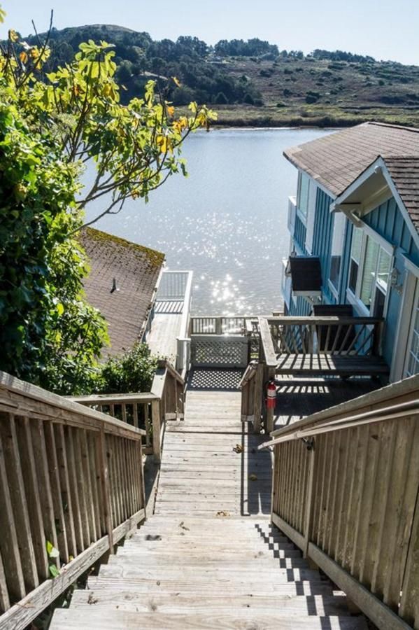 Wooden stairs leading down to a waterfront deck, with blue house and water view.